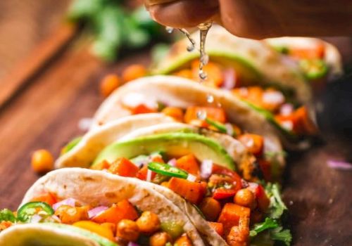 Soft tacos filled with chickpeas, vegetables, avocado slices, and garnished with fresh lime juice being squeezed on top.