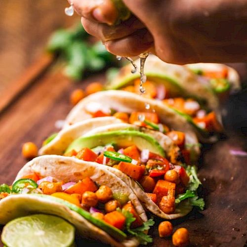 Soft tacos filled with chickpeas, vegetables, avocado slices, and garnished with fresh lime juice being squeezed on top.