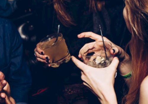People are enjoying drinks and laughing in a lively setting, with hands holding glasses and lively expressions evident.