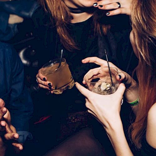 People are enjoying drinks and laughing in a lively setting, with hands holding glasses and lively expressions evident.