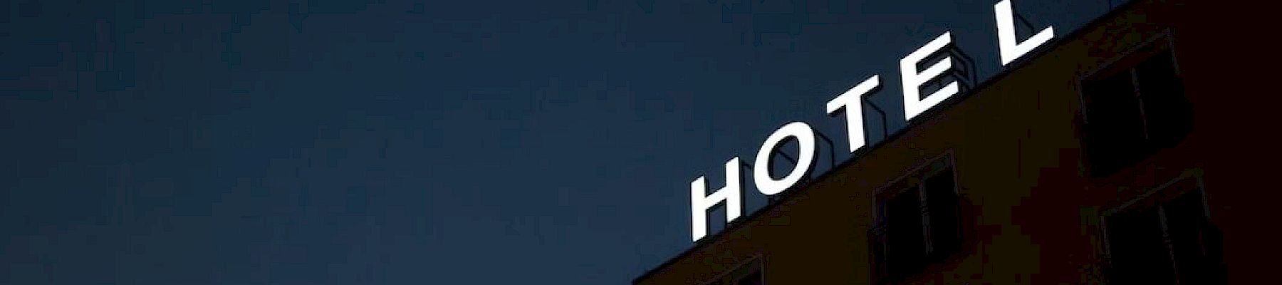 A building with an illuminated "HOTEL" sign, but the letter "H" is missing, against a dark sky background.