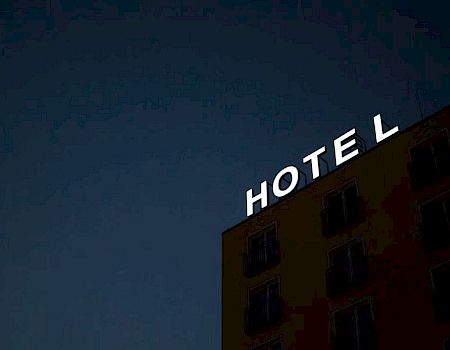 A building with an illuminated "HOTEL" sign, but the letter "H" is missing, against a dark sky background.